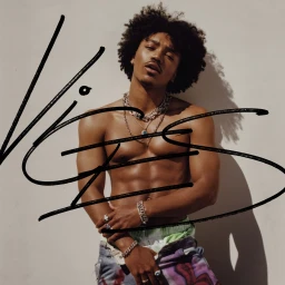 Portrait of a shirtless young Black man wearing layered silver chains and patterned jeans against a neutral wall, photographed by Blair Caldwell