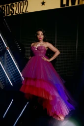 Taraji P. Henson in a strapless tiered magenta and purple tulle gown standing against a dark slatted background