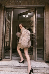 Woman in fluffy fur jacket stepping through a glass building entrance wearing black heels