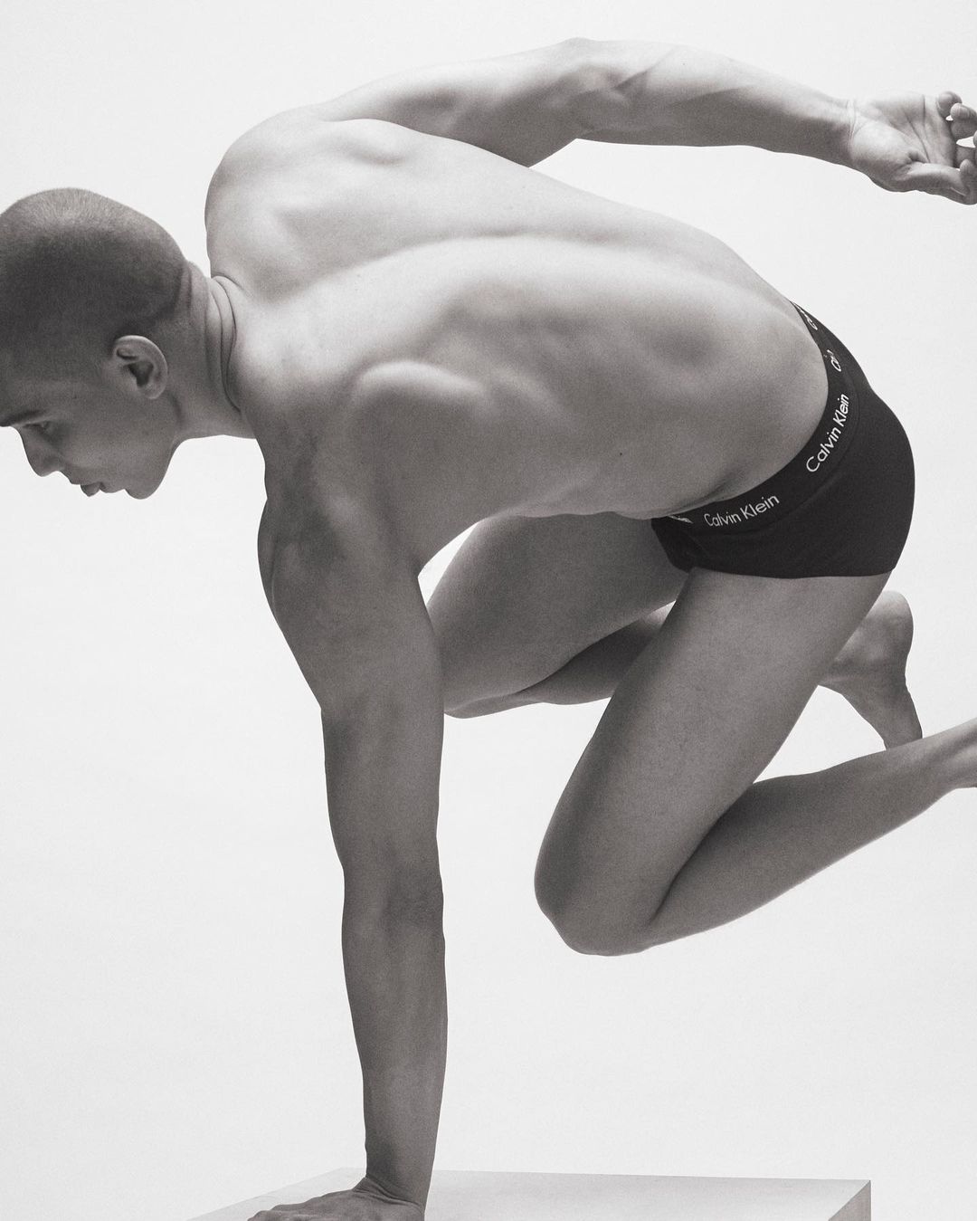 Athletic man in motion wearing Calvin Klein underwear, posing against a white backdrop. Striking black and white studio shot.