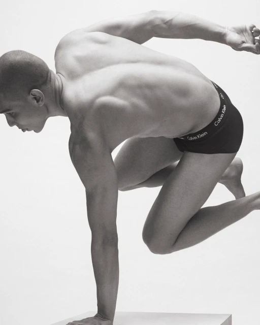 Athletic man in motion wearing Calvin Klein underwear, posing against a white backdrop. Striking black and white studio shot.