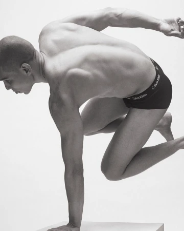 Athletic man in motion wearing Calvin Klein underwear, posing against a white backdrop. Striking black and white studio shot.