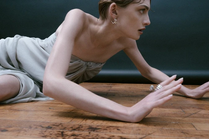 Model in strapless grey dress crouching on a wooden floor against a dark background, captured by Isaac Anthony.
