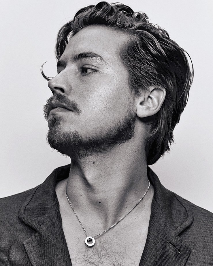 Black-and-white portrait of an adult male with dark wavy hair, a goatee, and a blazer, looking off to the side against a white backdrop.
