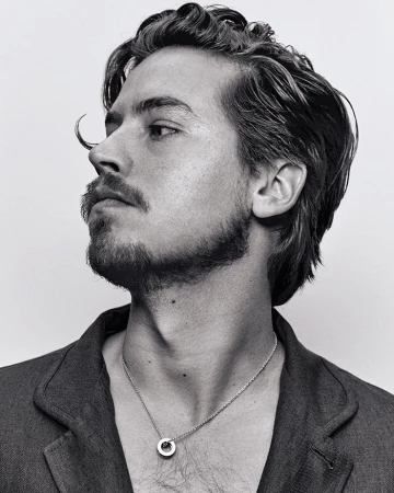 Black-and-white portrait of an adult male with dark wavy hair, a goatee, and a blazer, looking off to the side against a white backdrop.
