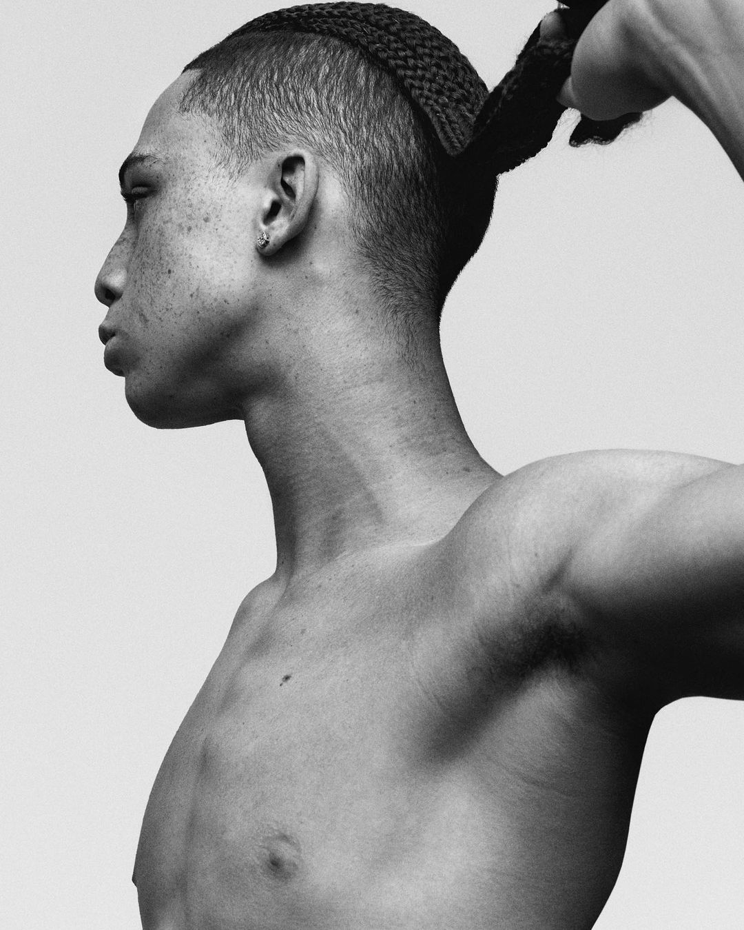 Monochrome portrait of shirtless Black male with braided hair, head in profile against a neutral backdrop, beauty and fashion portrait.