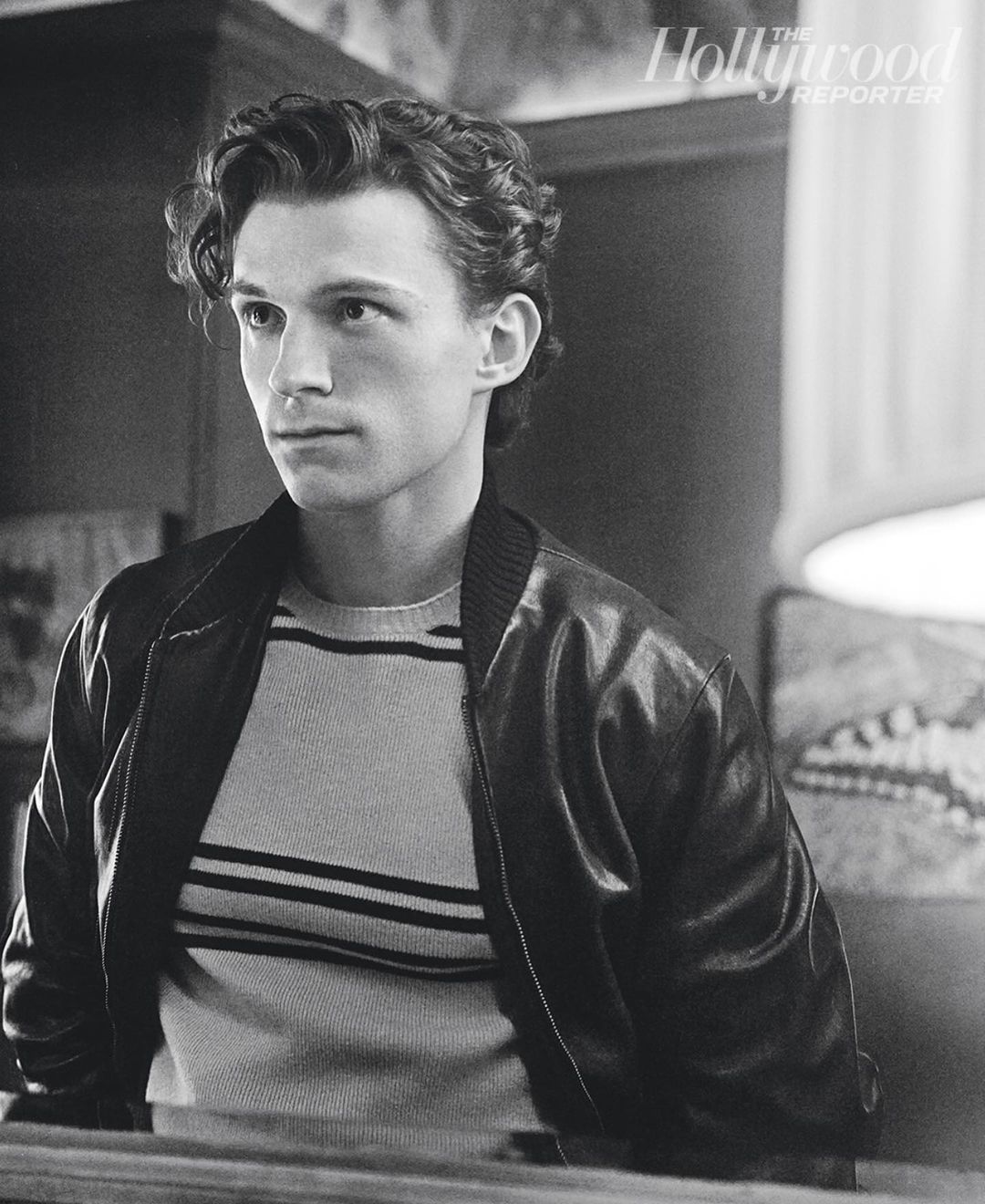 Monochrome portrait of adult male in striped sweater and bomber jacket, styled with curly hair and side glance. 'The Hollywood Reporter' logo.