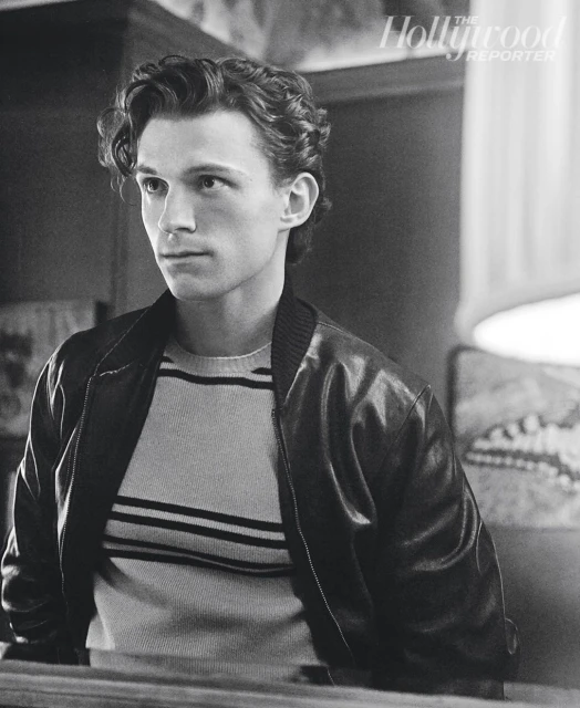 Monochrome portrait of adult male in striped sweater and bomber jacket, styled with curly hair and side glance. 'The Hollywood Reporter' logo.