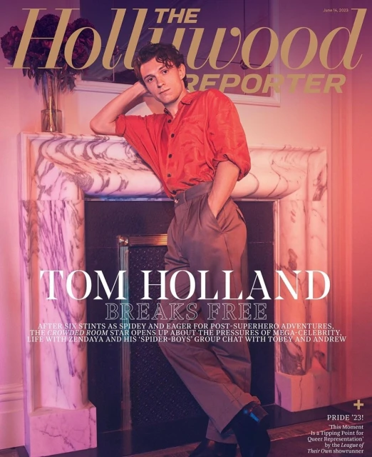 Magazine cover featuring Tom Holland in an unbuttoned red shirt and pleated slacks, leaning against a white marble fireplace mantel.