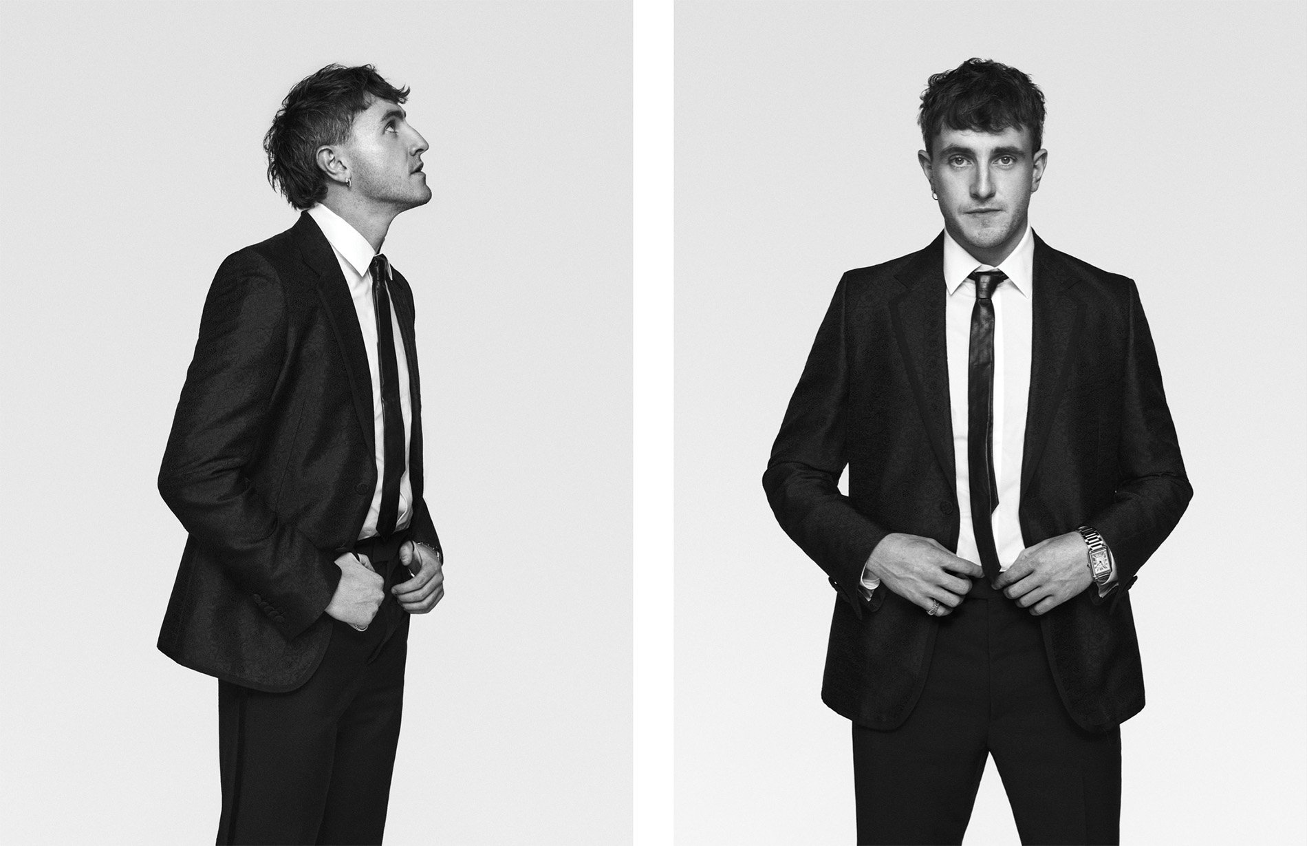 Black and white portrait of a man in a suit, looking up in profile and standing in front-facing view, wearing a tie and dress watch.