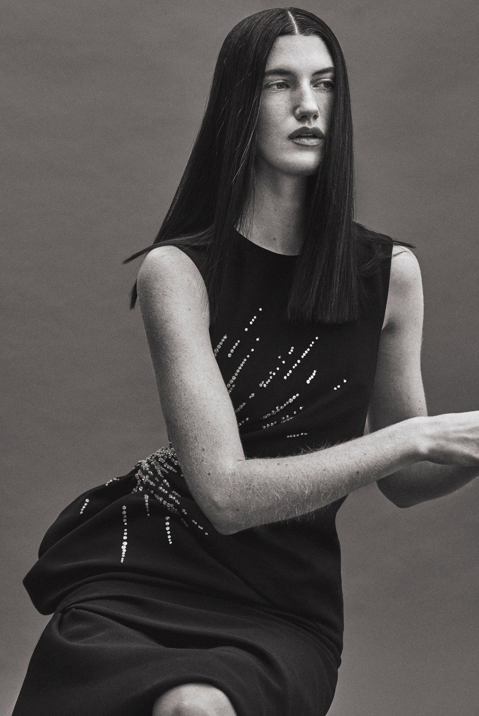Model with long dark hair wearing a black sleeveless dress against a grey backdrop captured by Isaac Anthony.