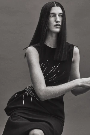 Model with long dark hair wearing a black sleeveless dress against a grey backdrop captured by Isaac Anthony.