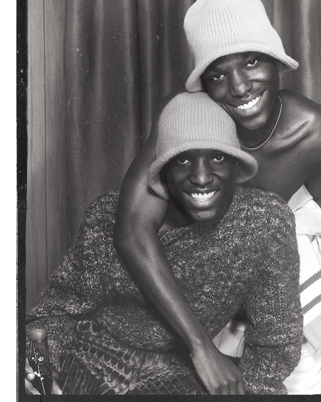 Black and white portrait of two Black adult males wearing hats and smiling, with one individual's arm around the other's shoulder.