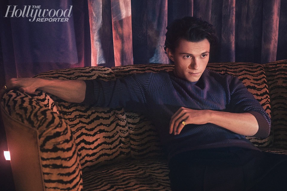 Candid portrait of a stylish male model posing on an animal-print couch in dim indoor light with The Hollywood Reporter logo in view.