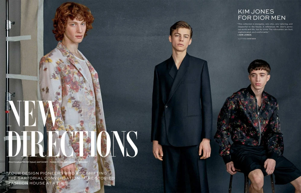 Fashion editorial shot of three young adult male models posing indoors against a grey backdrop, showcasing floral blazers and suits.