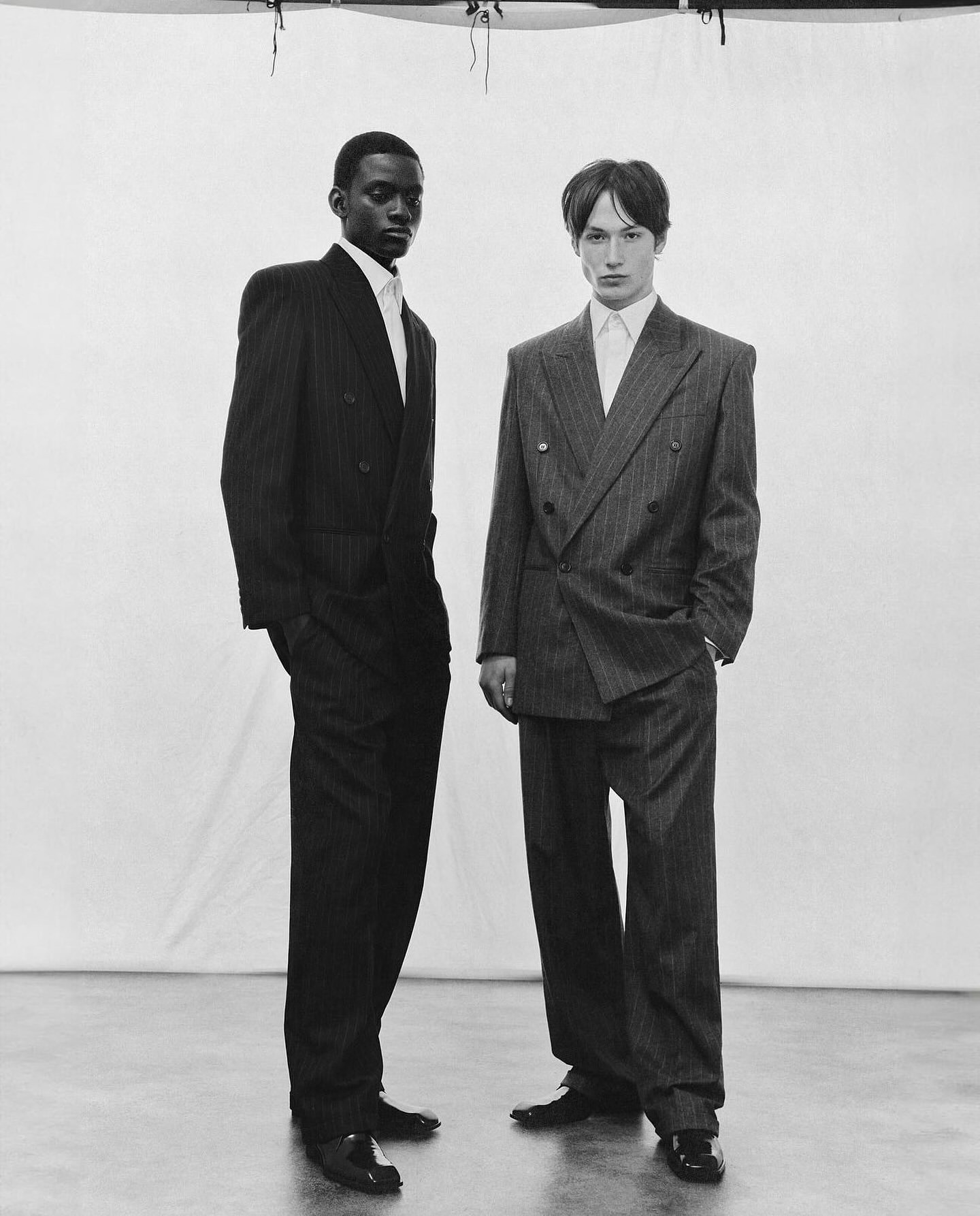 Two fashionable men in striped suits pose in a black and white studio portrait. Menswear fashion shoot with formal attire.