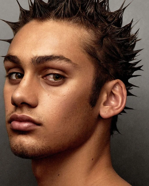 Close-up studio portrait of a young adult male with short, spiky brown hair. He gazes at the viewer with a neutral expression.