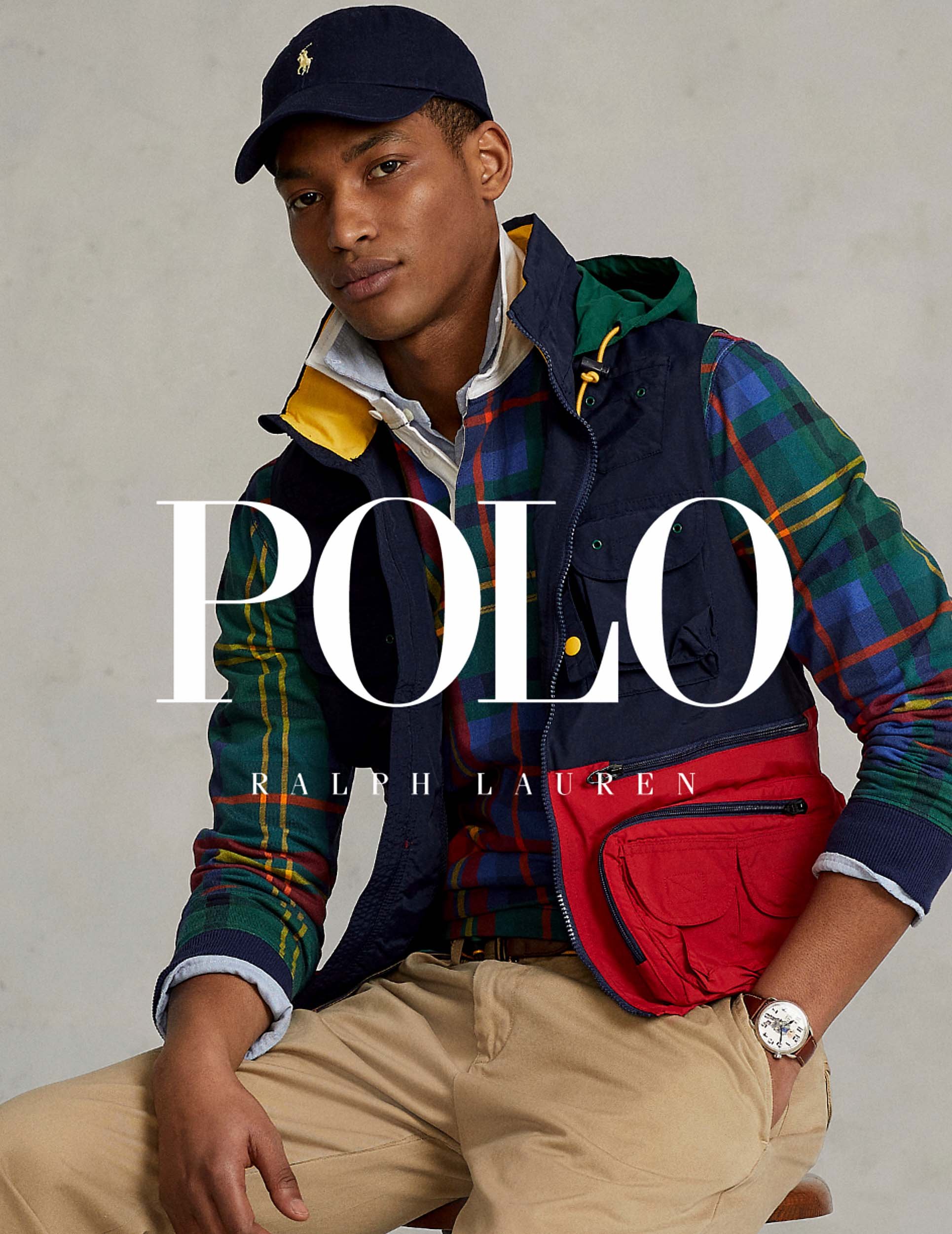 An adult male model wears a plaid flannel shirt layered with a navy vest and khaki pants, posing in a bright studio for Polo Ralph Lauren.