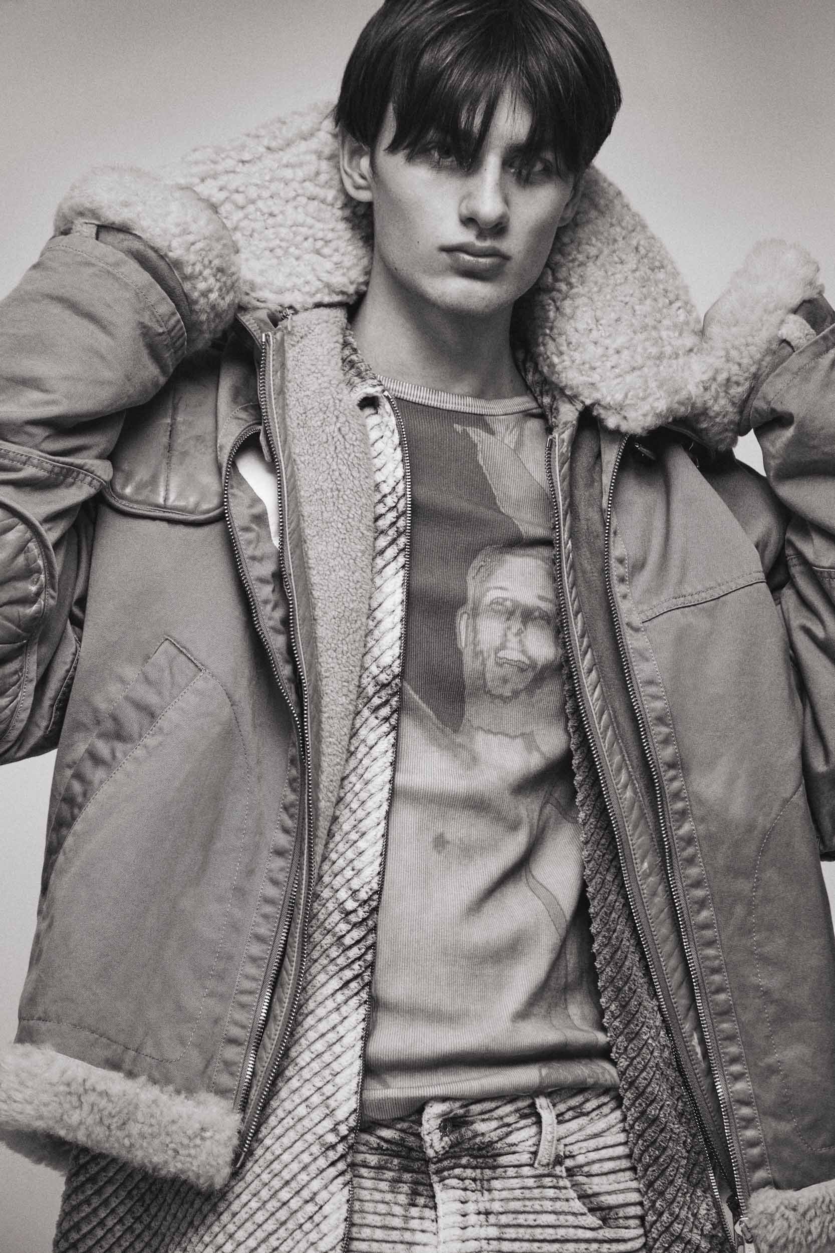 Monochrome portrait of a young male model wearing a heavy shearling-lined jacket and patterned t-shirt by Isaac Anthony.