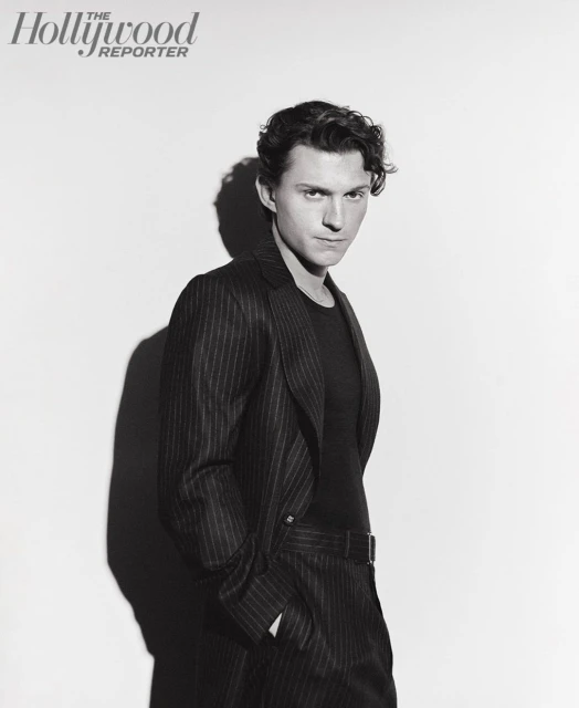 Black and white portrait of a young adult male in a pinstripe suit jacket and dark shirt, posing against a white backdrop in a photo studio.