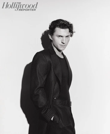 Black and white portrait of a young adult male in a pinstripe suit jacket and dark shirt, posing against a white backdrop in a photo studio.