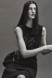 Model with long dark hair wearing a black sleeveless dress against a grey backdrop captured by Isaac Anthony.