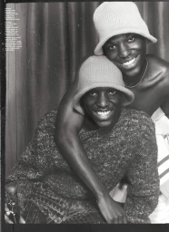 Two smiling Black men wearing bucket hats and knitted sweaters posing together in a monochrome editorial portrait.