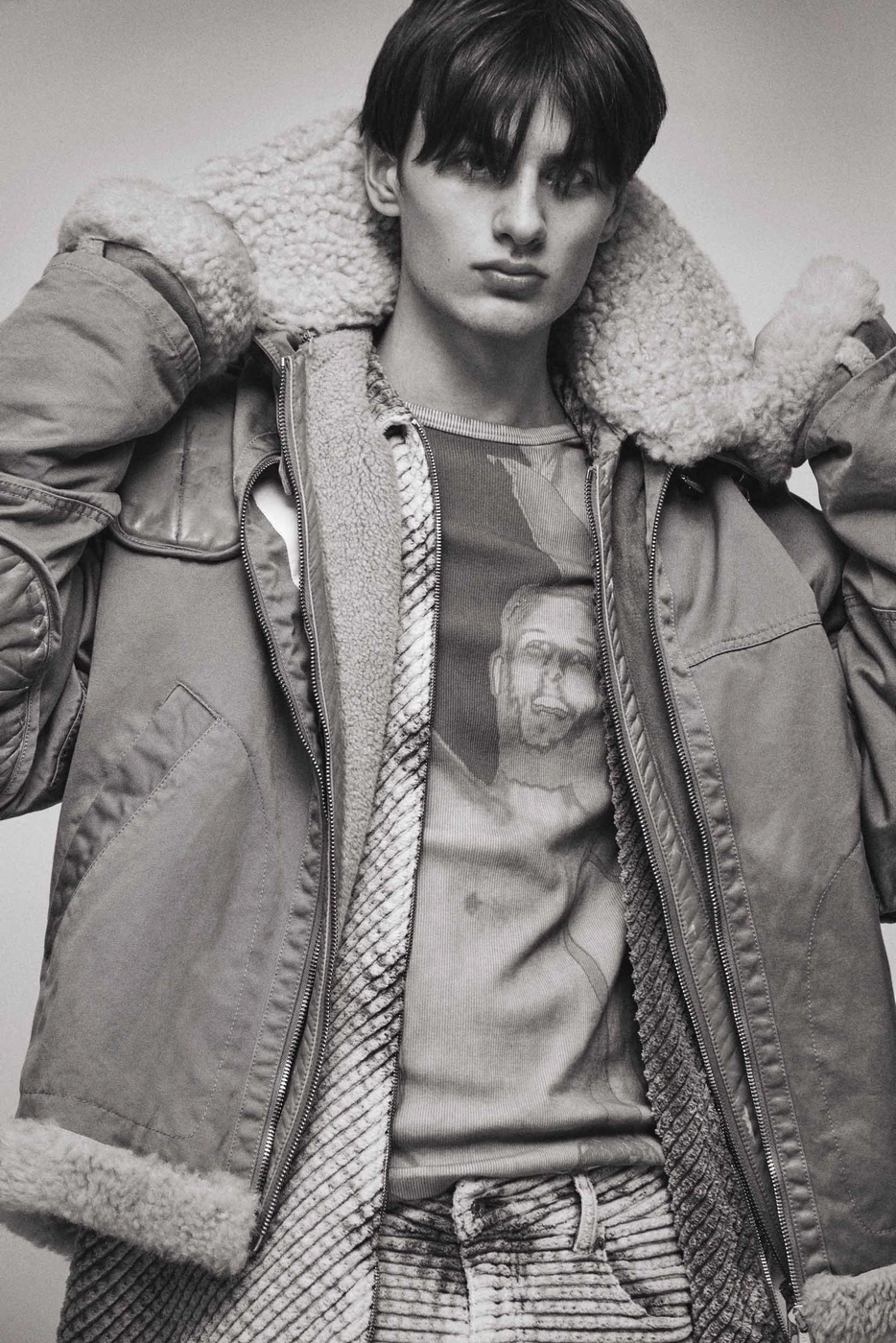 Monochrome portrait of a young male model wearing a heavy shearling-lined jacket and patterned t-shirt by Isaac Anthony.