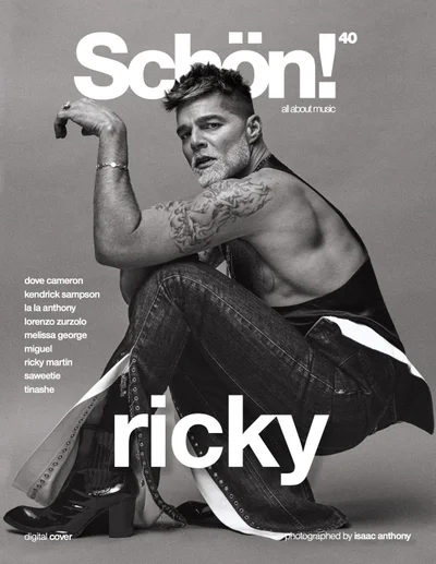 Monochrome magazine cover portrait of Ricky Martin squatting in dark denim pants and black top against a grey backdrop