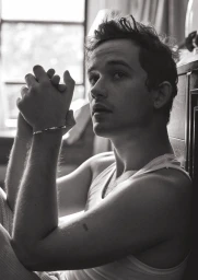 Monochrome portrait of a young man wearing a white tank top with clasped hands raised near his face.