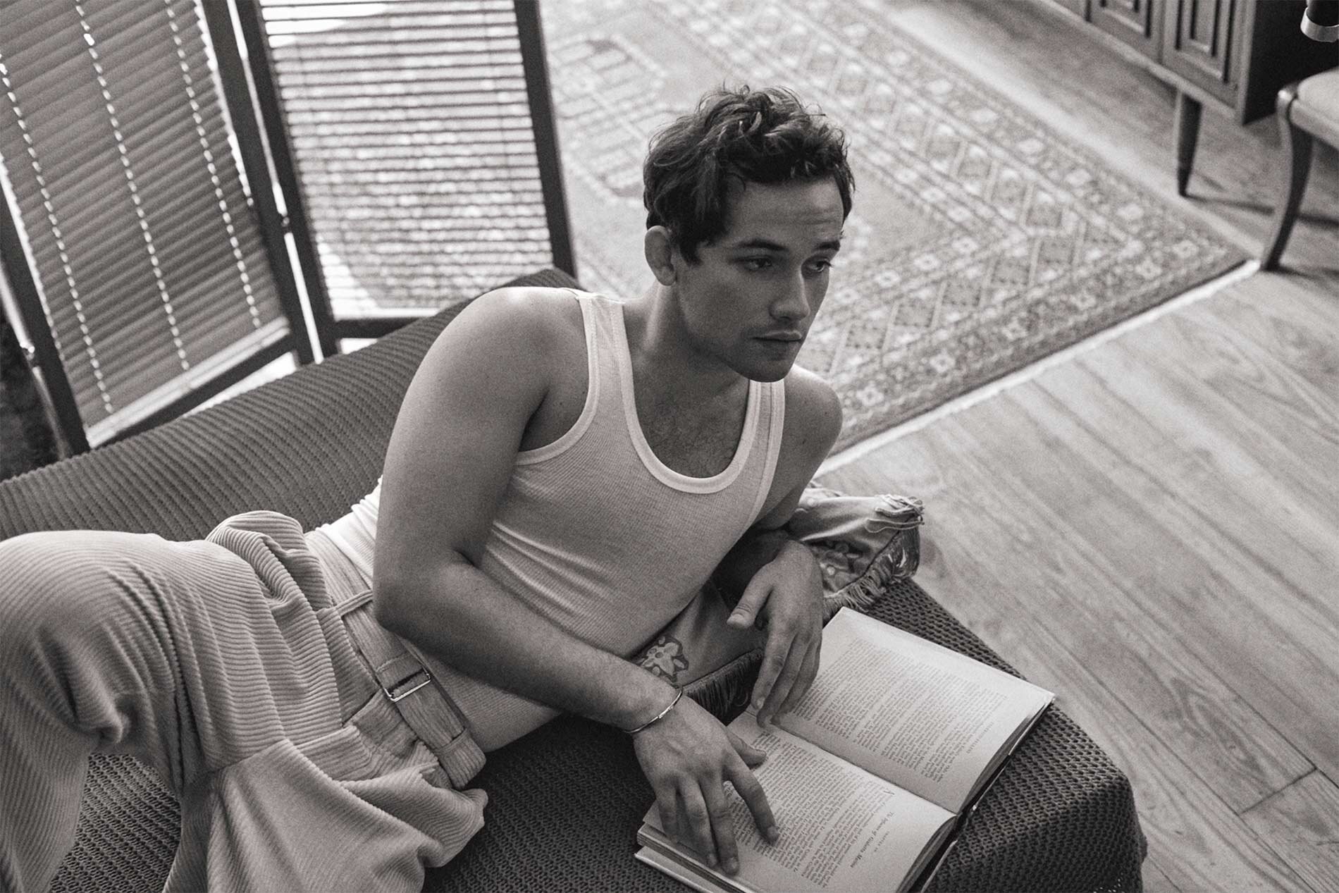 Monochrome portrait of a young man reclining on a sofa holding an open book, photographed by Isaac Anthony