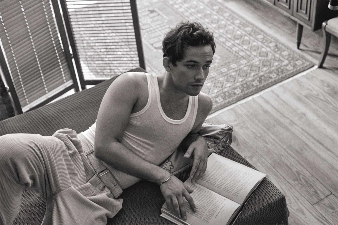 Monochrome portrait of a young man reclining on a sofa holding an open book, photographed by Isaac Anthony