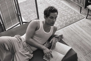 Monochrome portrait of a young man reclining on a sofa holding an open book, photographed by Isaac Anthony