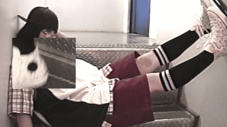 Person wearing dark cap, glasses, black socks and sneakers reclined on metal staircase with legs elevated against a wall.