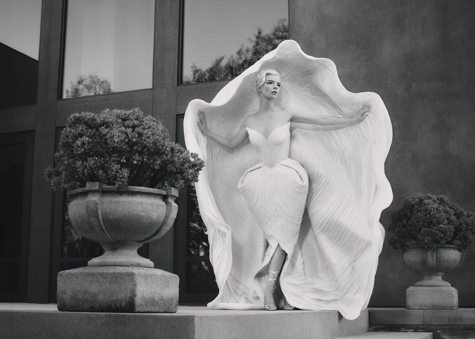 Woman wearing an avant-garde white sculpted dress standing on a terrace between two large stone planters