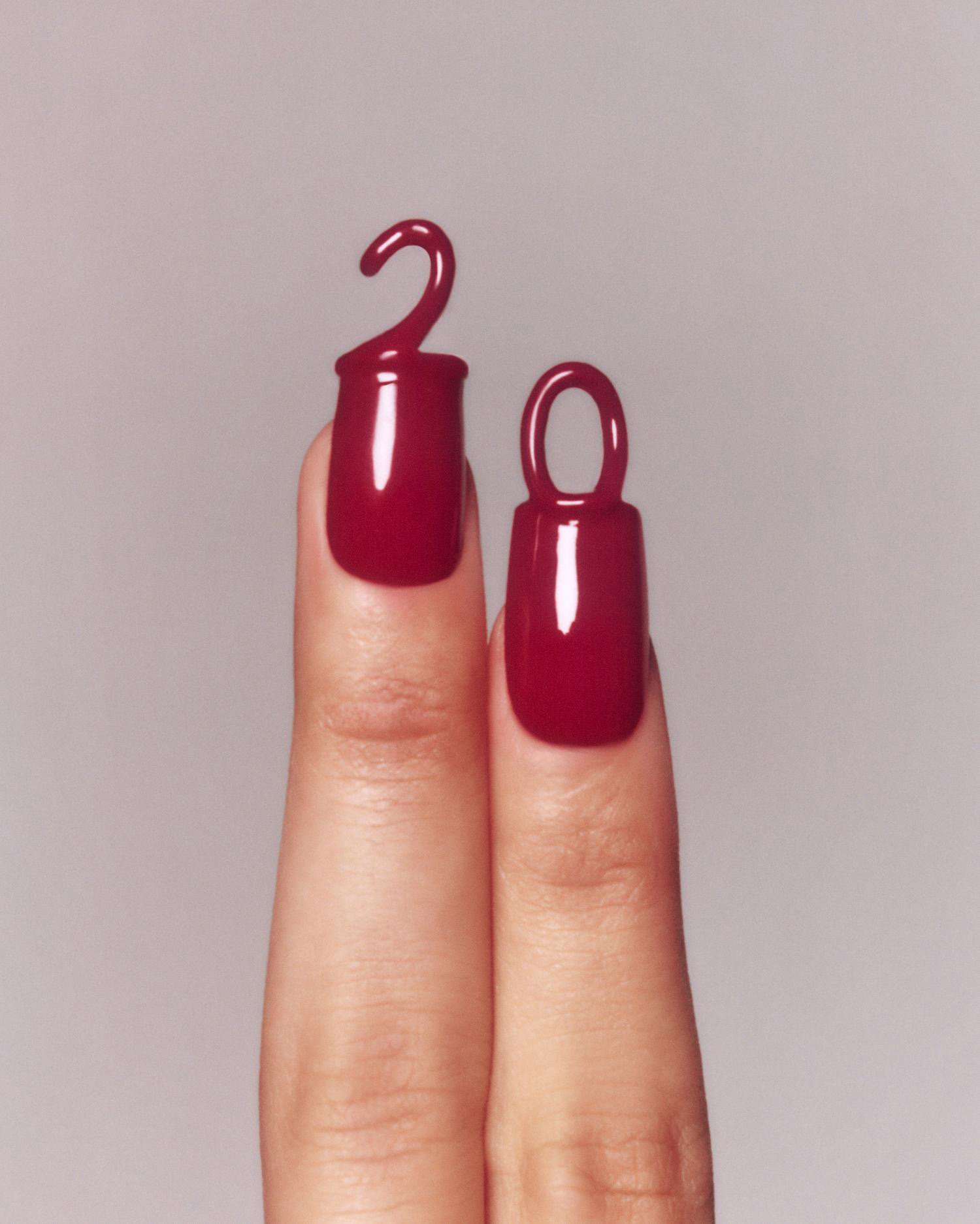 Close-up shot of two fingers featuring glossy, dark red nail polish with creative, elevated designs resembling small decorative shapes.