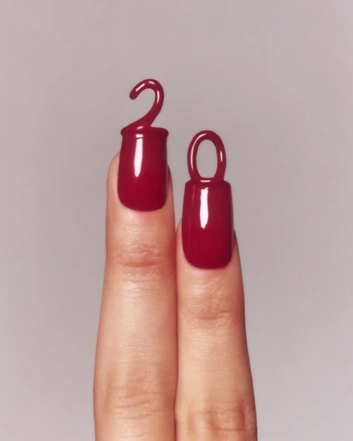 Close-up shot of two fingers featuring glossy, dark red nail polish with creative, elevated designs resembling small decorative shapes.