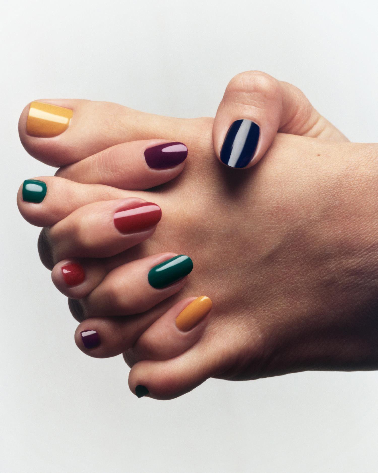Close-up of a fair-skinned woman's hands with a variety of nail polish colors, including yellow, red, green, purple, and striped.