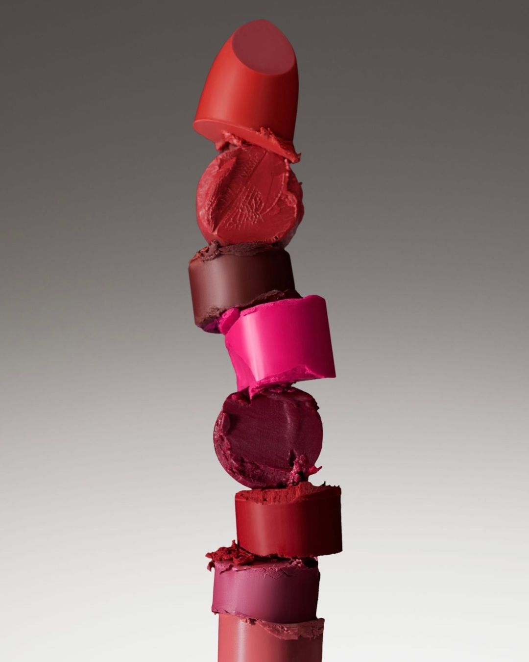 Stacked lipstick tower in various colors. Shades of red, pink, and purple cosmetic products form an abstract and colorful beauty display.