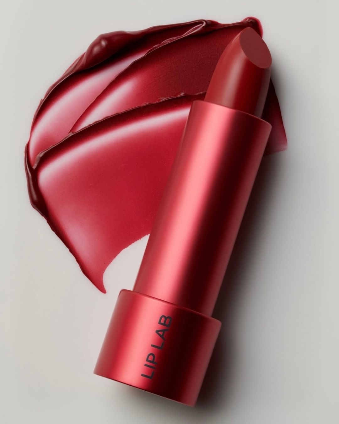 Red lipstick tube with smear on white background. Close-up shot of beauty and makeup product. Cosmetic still life.