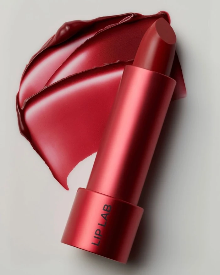 Red lipstick in a metallic red case set against a pale background with a glossy red lipstick swatch above it.