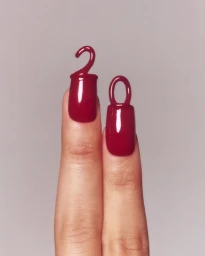 Close-up of two fingers with glossy red manicured nails featuring sculpted hook and loop extensions by Mario Kroes.