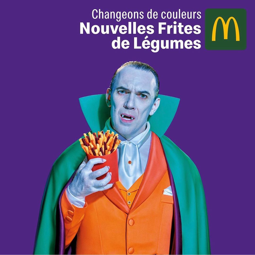 Man dressed as Dracula holds french fries. Advertisement for McDonald's veggie fries on purple background with company logo and text.