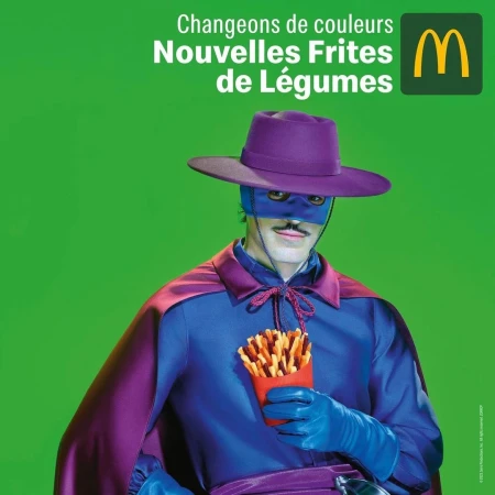 Person in Zorro-like costume holds a container of veggie fries against a bright green backdrop, promoting McDonald's new fries.