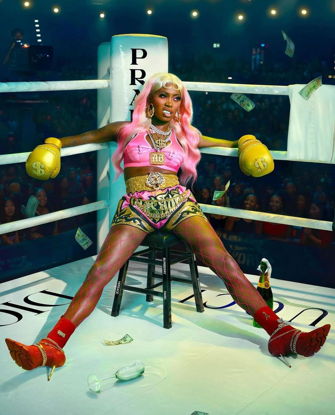 A confident woman in boxing attire sits in a boxing ring with money falling, champagne nearby, and a crowd in the background.