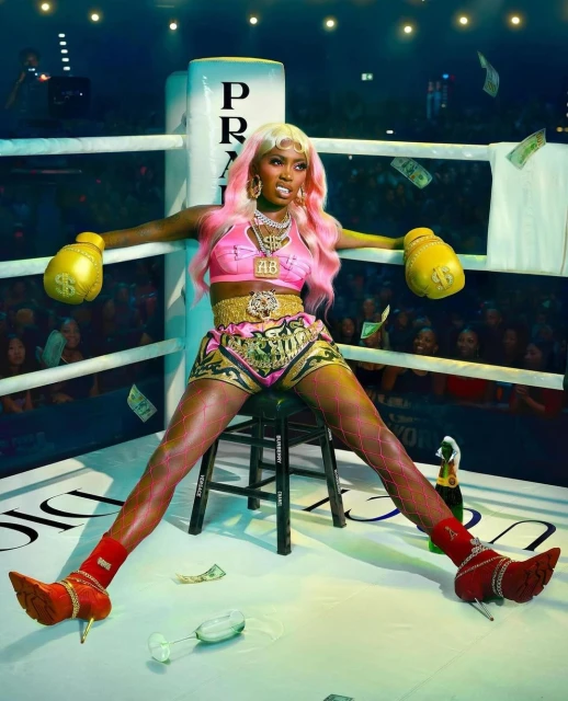 A confident woman in boxing attire sits in a boxing ring with money falling, champagne nearby, and a crowd in the background.