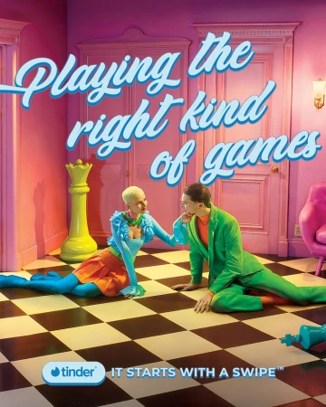 Whimsical dating app ad features a stylish couple on a checkered floor, chess pieces, and pastel furniture, all under bright studio lighting.