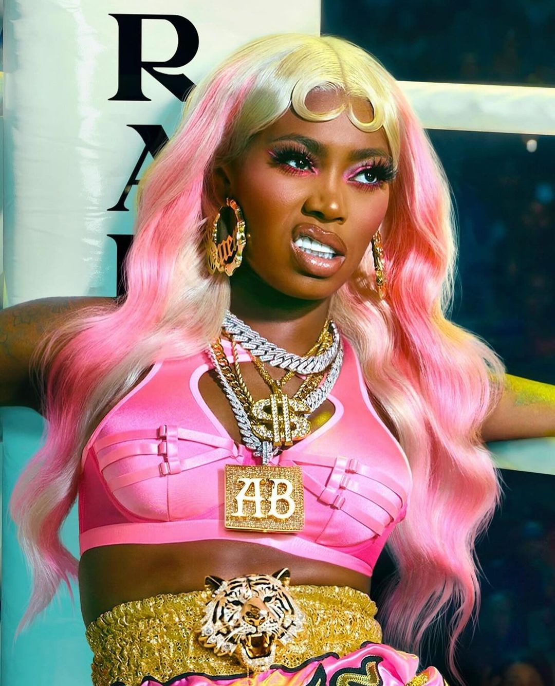 Glamorous African-American woman in pink boxing outfit with jewelry, fierce expression, against a studio boxing ring background.