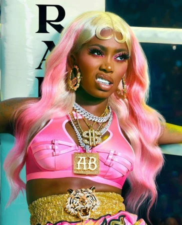 Glamorous African-American woman in pink boxing outfit with jewelry, fierce expression, against a studio boxing ring background.