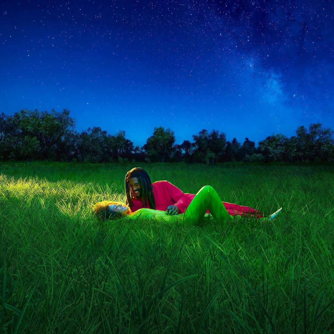 Two people, one adult man and one adult female, lying in a green grassy field underneath a starry night sky. Outdoor recreation.